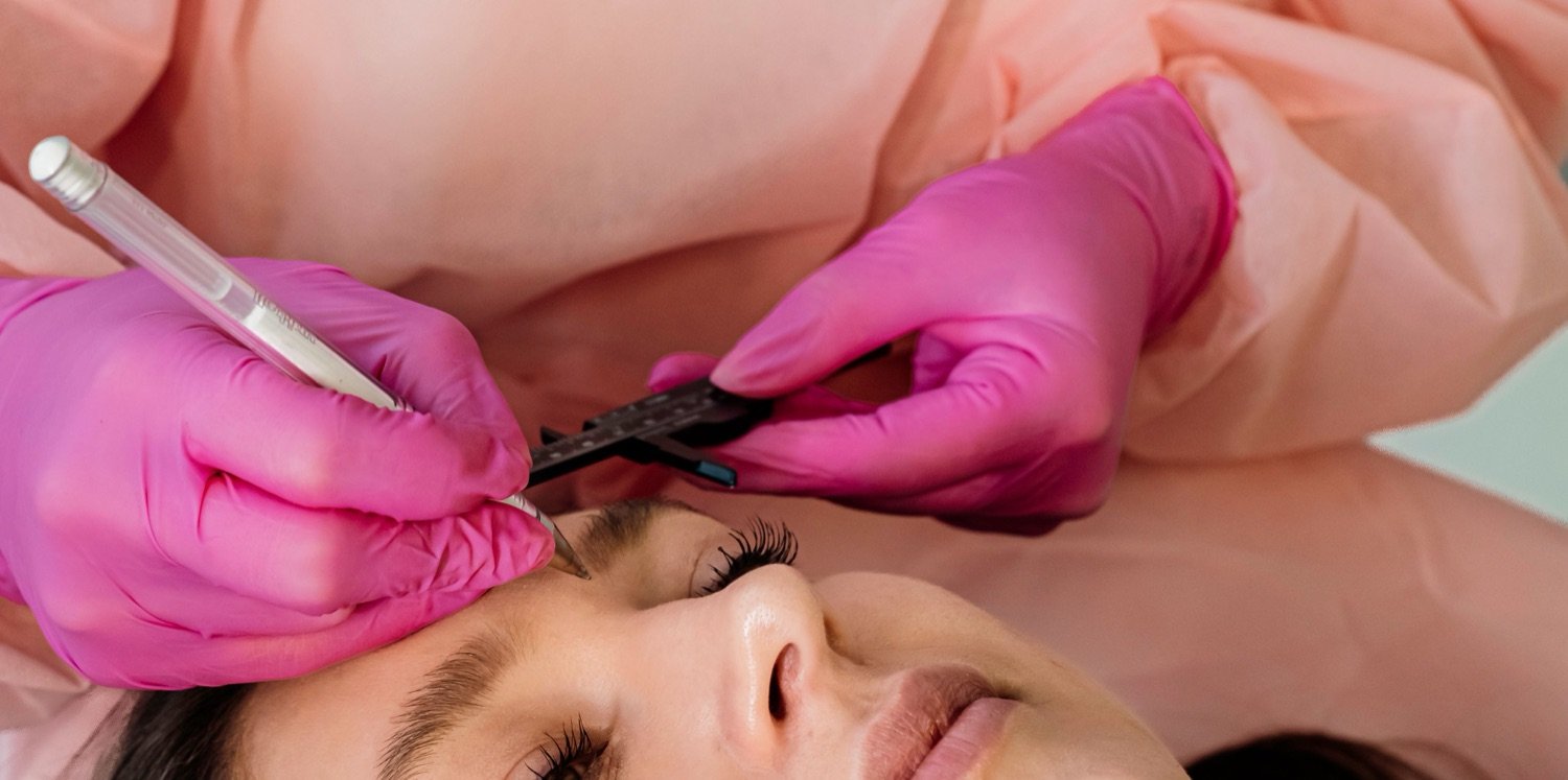 Relaxed client having her eyebrows shaped by a gloved beautician